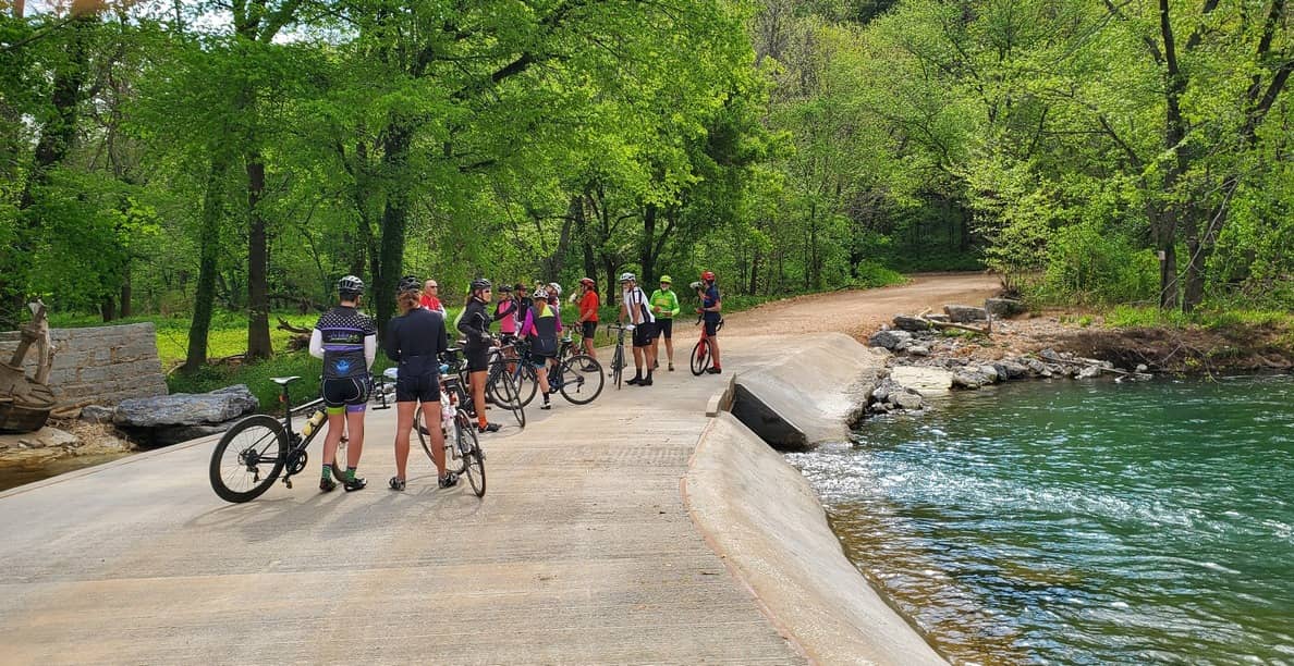 group of cyclists pausing to rest and talk on a short bridge