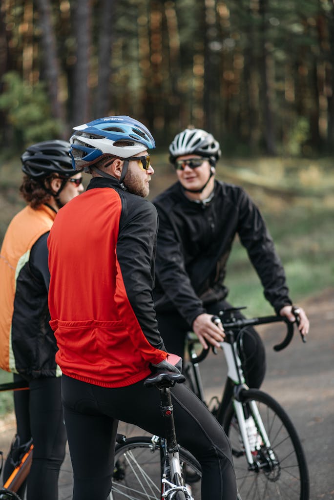 Three cyclists taking a break on a forest path, wearing protective gear and having a conversation.